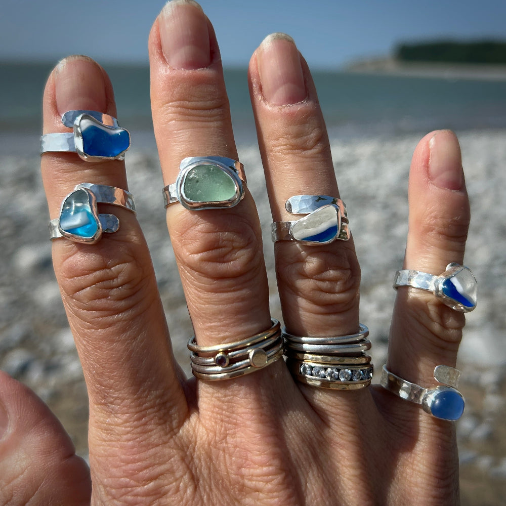 Hand wearing multiple silver rings with gemstones against a beach background