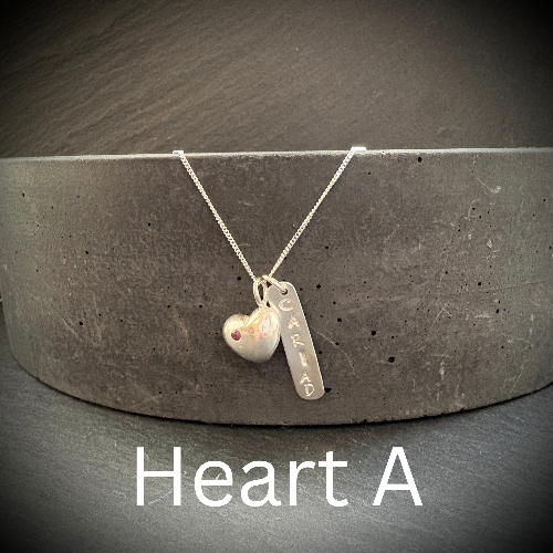 Silver necklace with heart pendant and engraved tag on a dark surface
