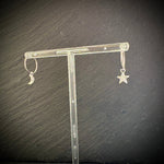 Silver earrings with star and moon designs on a clear stand against a dark background