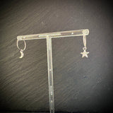Silver earrings with star and moon designs on a clear stand against a dark background