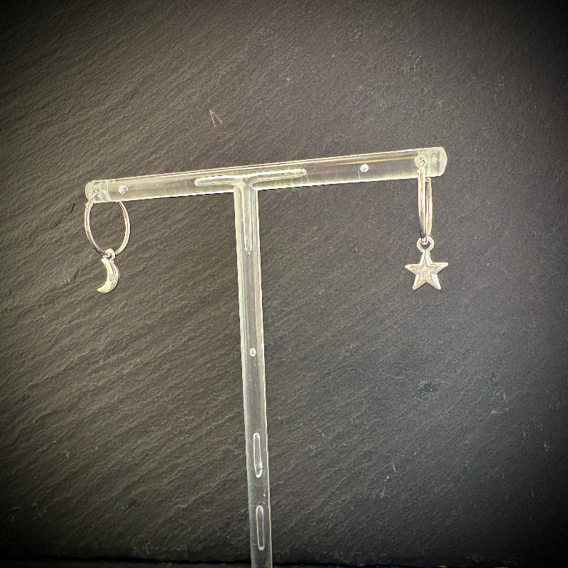 Silver earrings with star and moon designs on a clear stand against a dark background