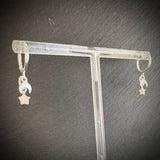 Silver earrings with star and moon designs on a clear stand against a dark background