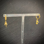 Gold earrings on a clear T-shaped stand against a dark background