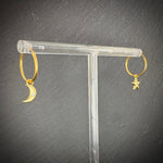 Gold hoop earrings with moon and star designs on a clear stand against a dark background