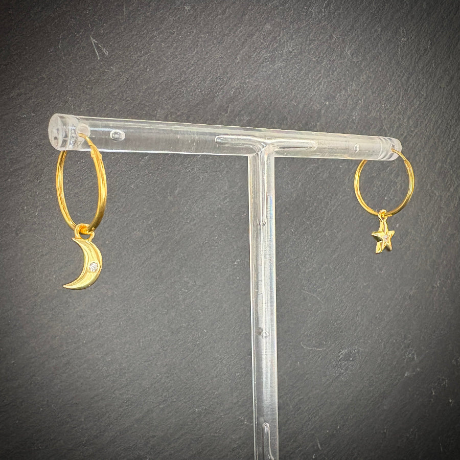 Gold hoop earrings with moon and star designs on a clear stand against a dark background