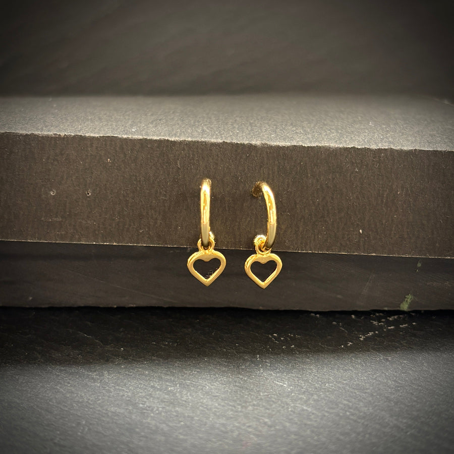 Gold heart-shaped hoop earrings on a dark surface