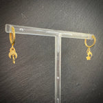 Gold hoop earrings with moon and star charms on a clear stand against a dark background