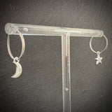 Silver hoop earrings with moon and star charms on a clear stand against a dark background