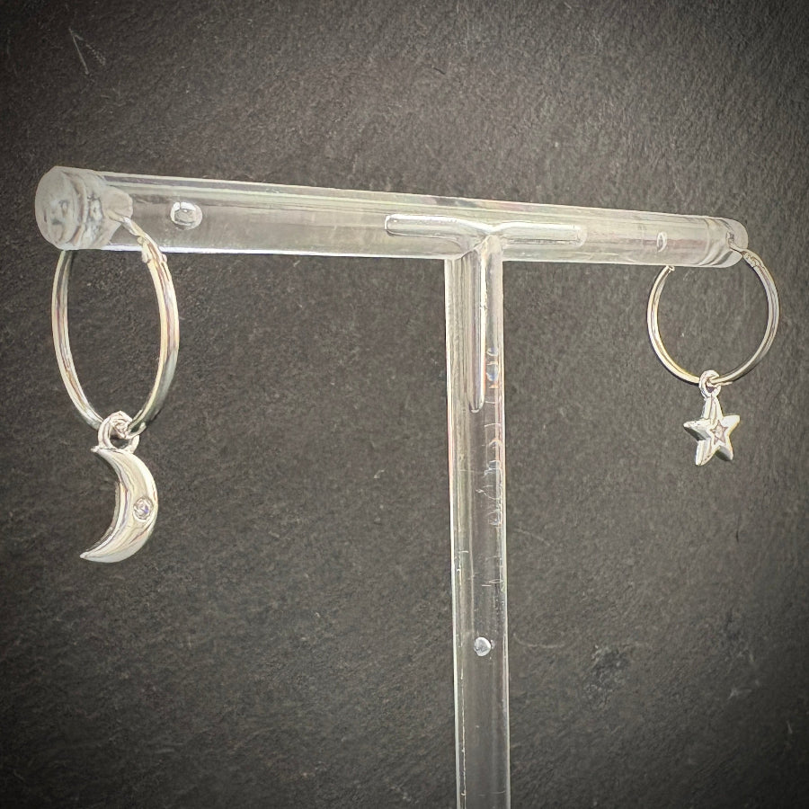 Silver hoop earrings with moon and star charms on a clear stand against a dark background