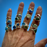 Hand wearing multiple Sterling silver rings with colourful seaglass against a blue sky