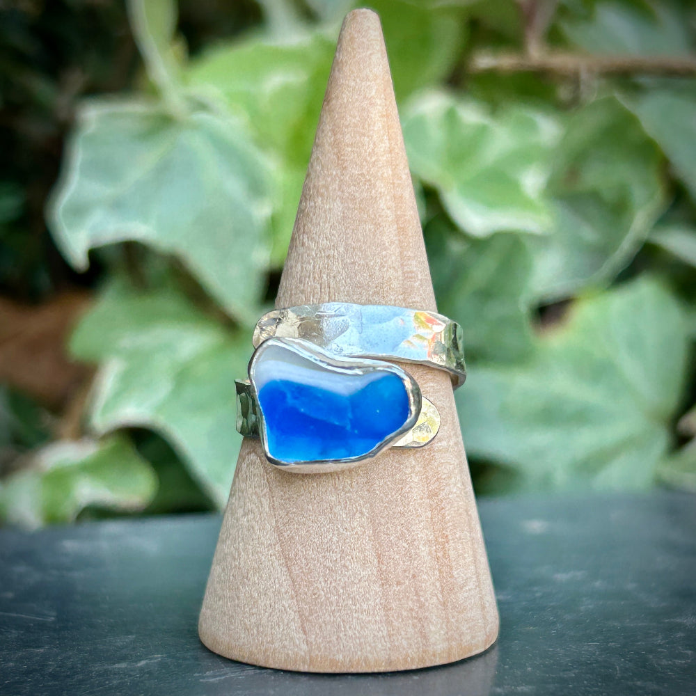 Silver Ring with blue Sea Glass on a wooden cone against a green leafy background
