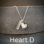 Necklace with solid sterling silver heart-shaped pendant and inset ruby and engraved love tag on a dark surface