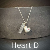 Necklace with solid sterling silver heart-shaped pendant and inset ruby and engraved love tag on a dark surface