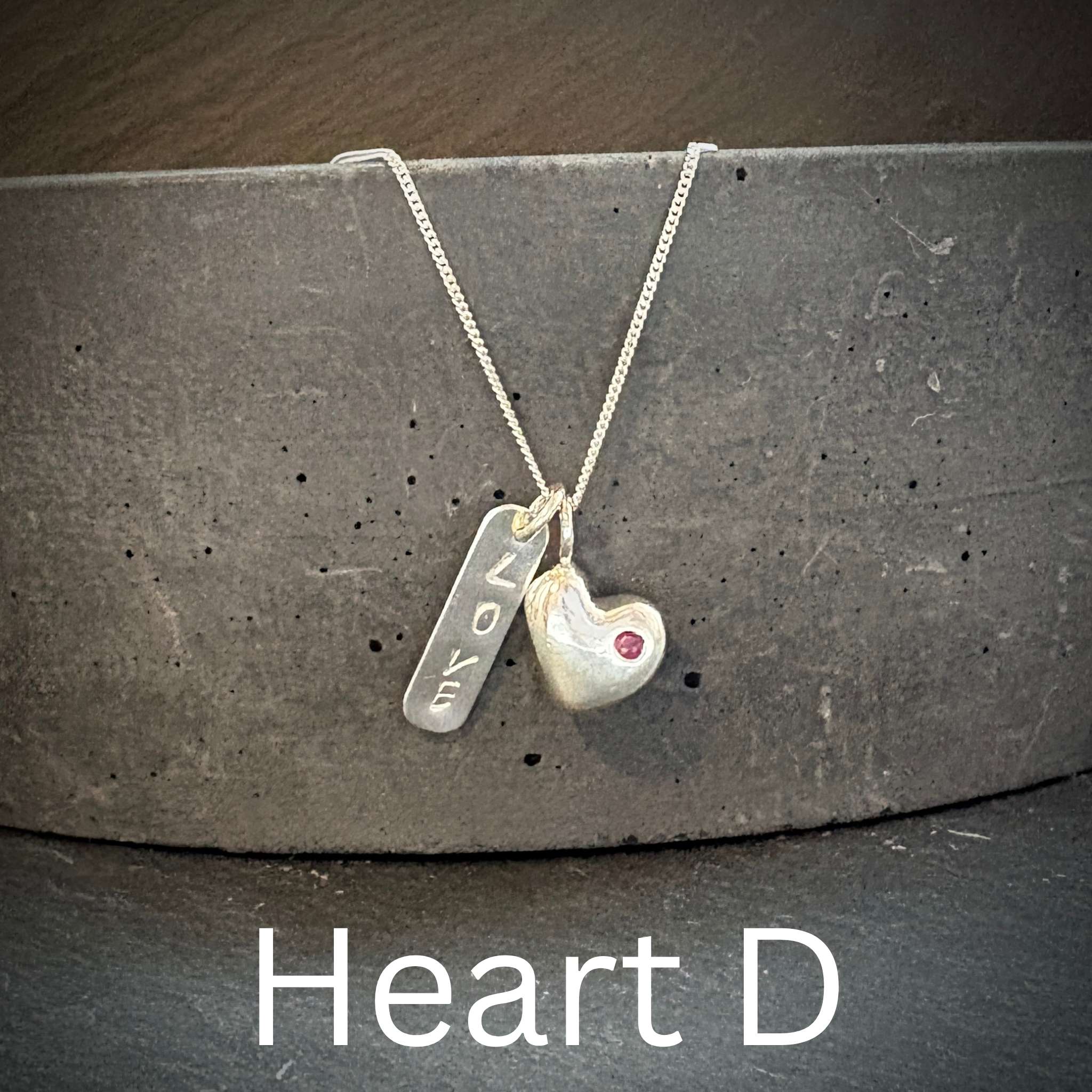 Necklace with solid sterling silver heart-shaped pendant and inset ruby and engraved love tag on a dark surface