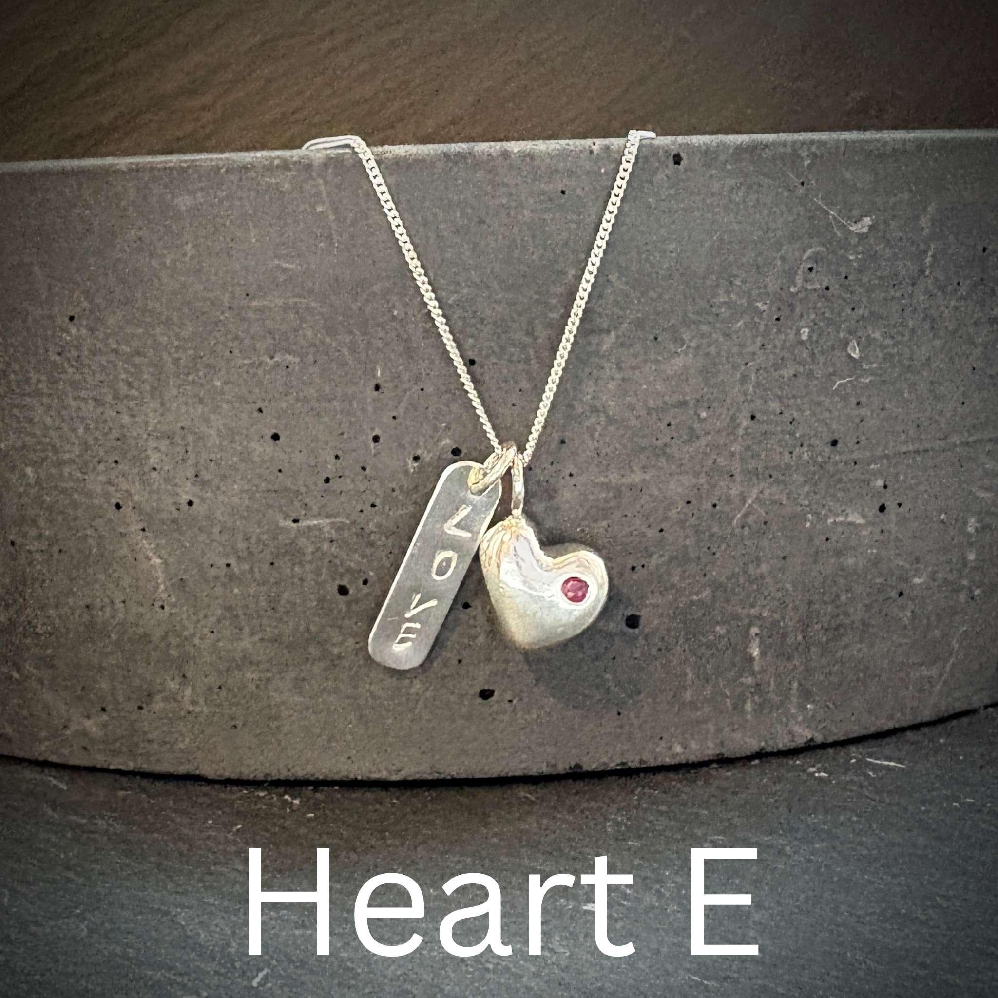 Necklace with solid silver heart-shaped pendant and engraved love tag on a dark surface